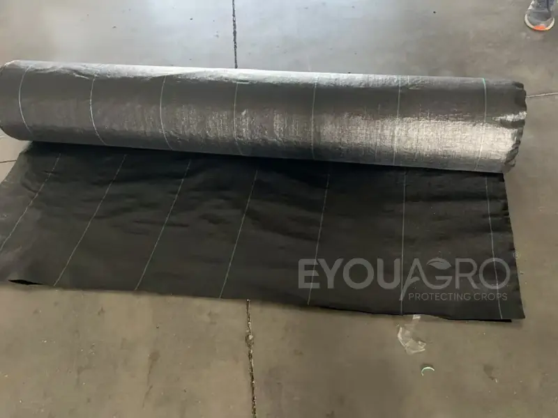A wide loom at the EyouAgro factory weaving black ground cover weed mat with green guide lines.
