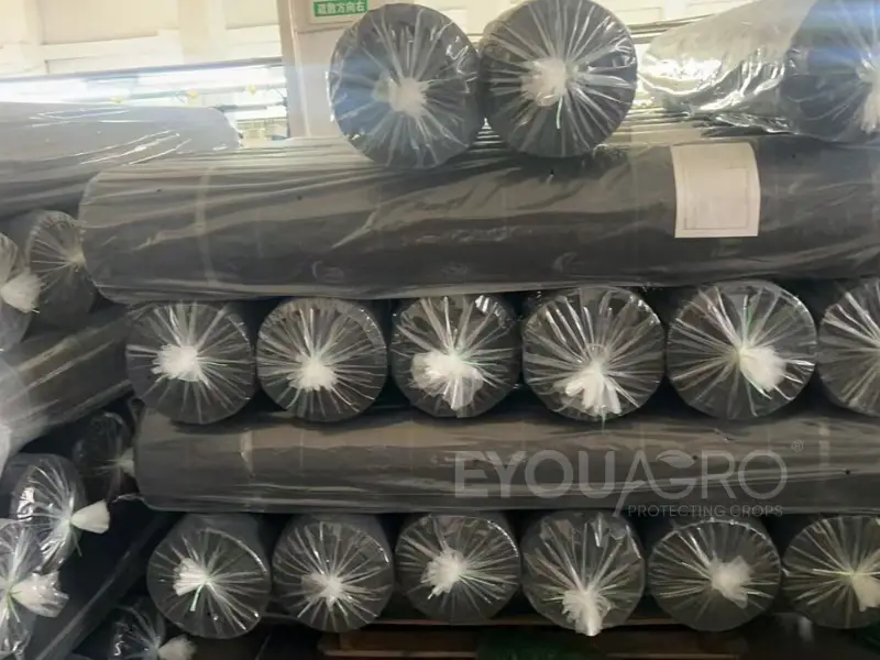 Tightly packed rolls of woven weed mat next to a box of heavy-duty ground pegs.