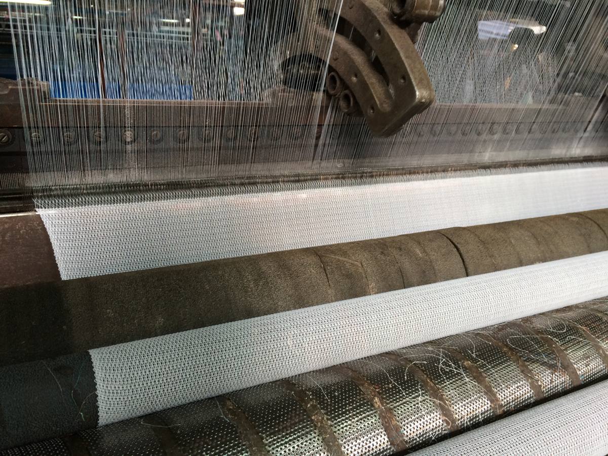 Raschel knitting machine with warp yarns feeding the finished white mesh