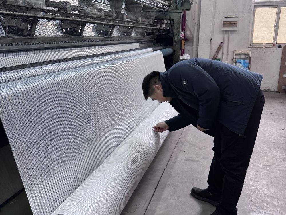 Técnico verificando a tela aluminizada que sai da máquina de tricô por urdidura.